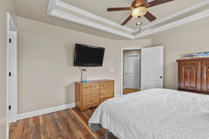 Tray ceiling with crown molding, wood-finish flooring, ceiling fan with integrated lighting, and white interior doors