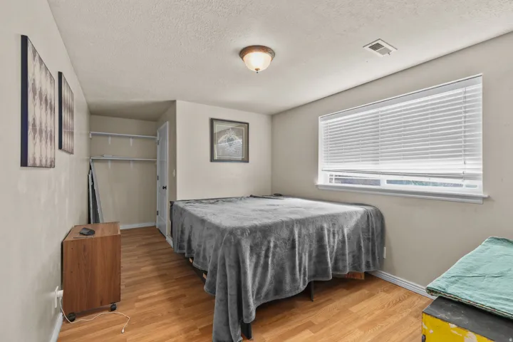 Room featuring wood-finish flooring, a window with horizontal blinds, and a built-in closet with shelving