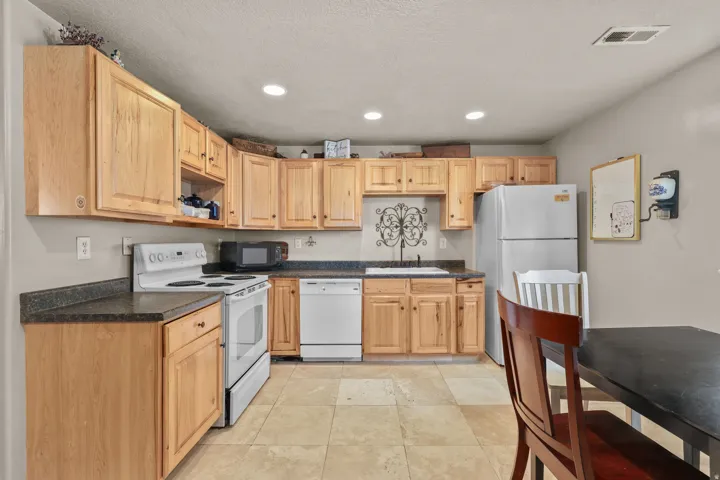 Kitchen featuring extensive wood cabinetry, dark countertops, a white electric range, a white dishwasher, and light-toned tile flooring