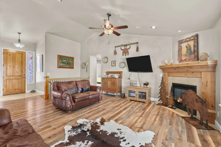 Vaulted ceiling with a ceiling fan, wood-finish flooring, built-in fireplace with a wood mantel, recessed lighting, and a wood entry door