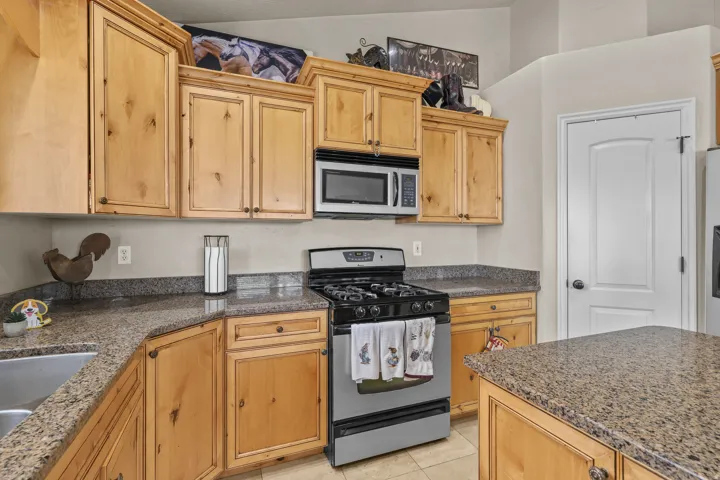 Kitchen featuring light wood-finish cabinetry, speckled countertops, a stainless steel gas range, and an integrated microwave