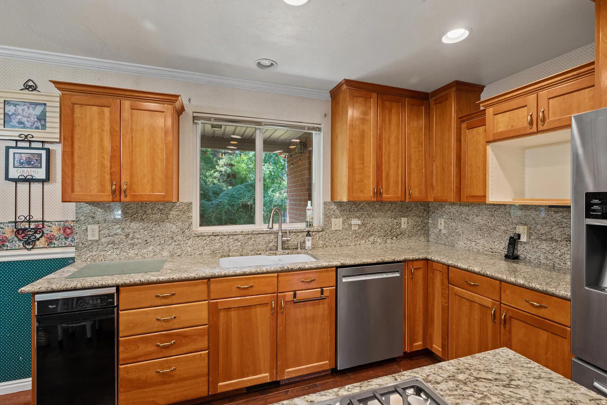 Kitchen featuring wood cabinetry, stone countertops, integrated sink with gooseneck faucet, stainless steel dishwasher, and a built-in cooktop