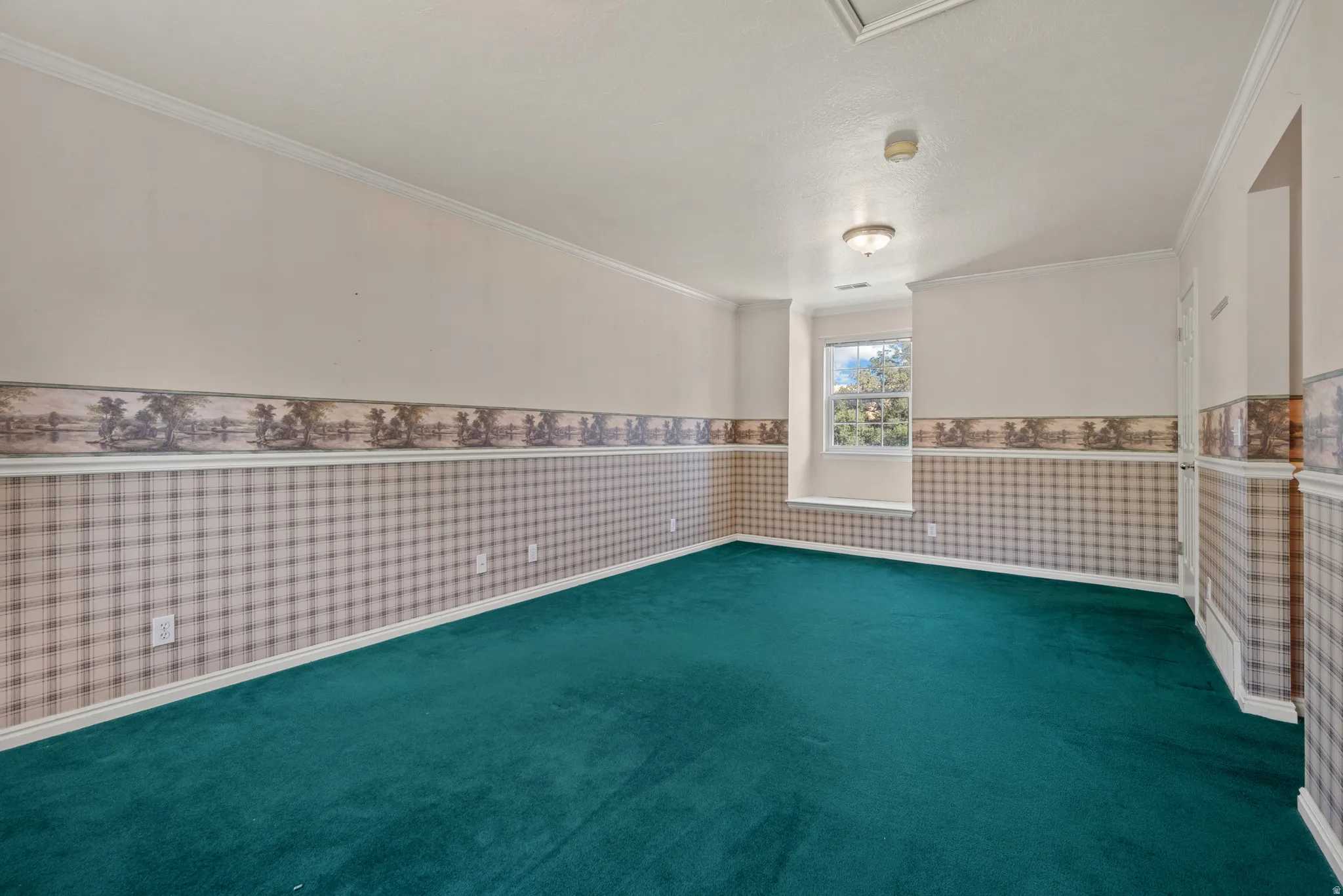 Spacious room featuring broadloom carpeting, a window, wall sconce, and crown molding