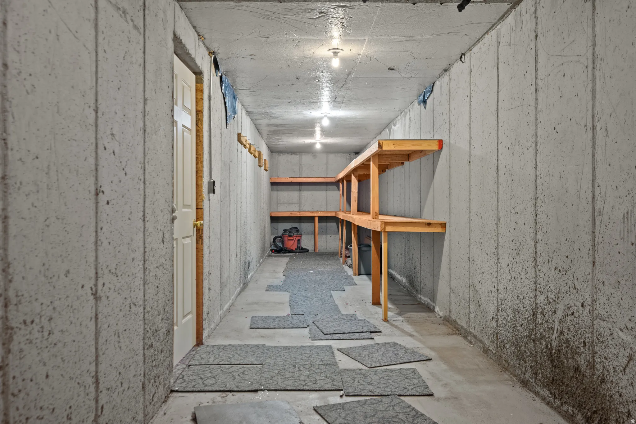 Concrete wall construction with built-in wooden shelving, recessed ceiling lighting, and a white paneled door