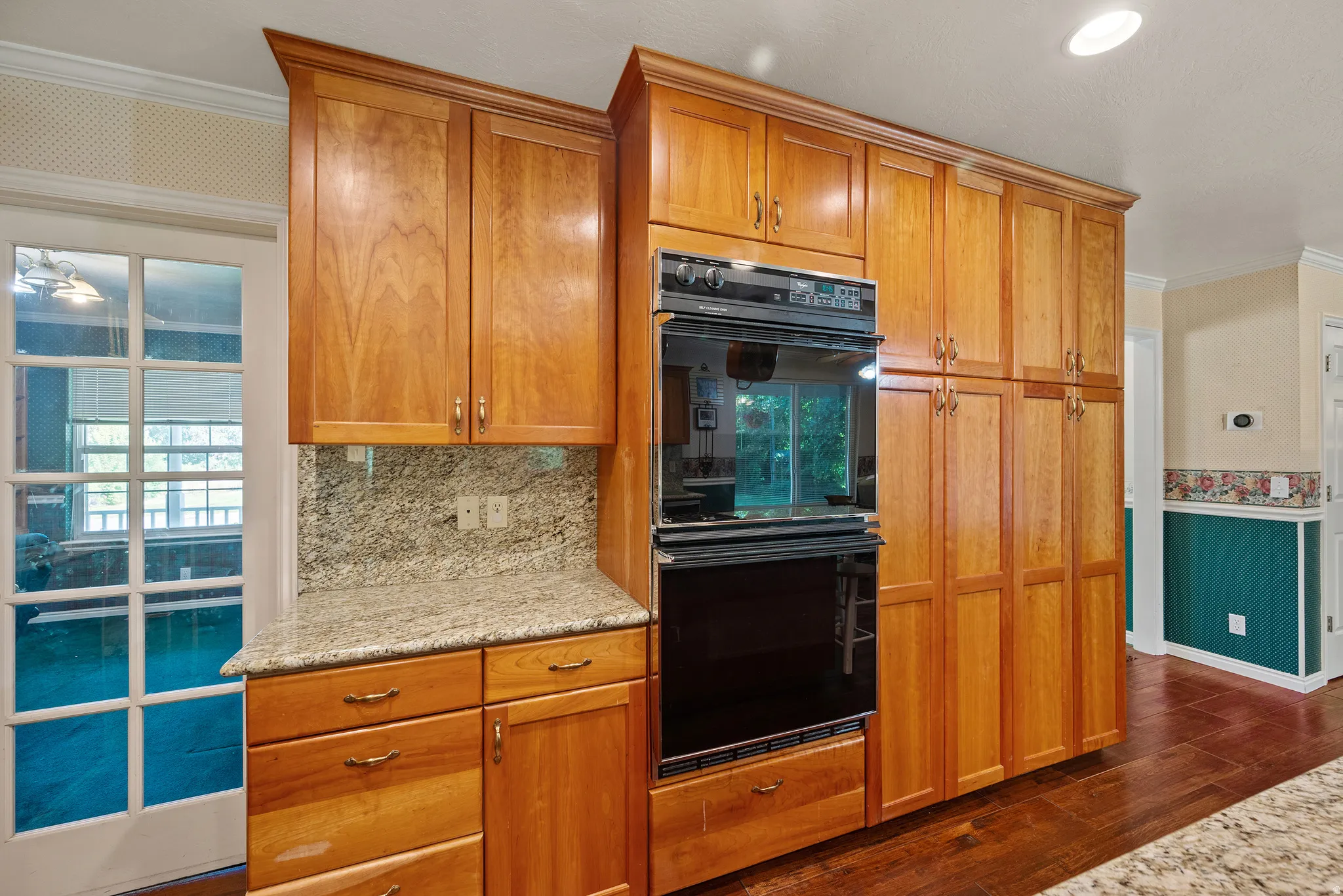 Built-in double oven, extensive cabinetry with wood finishes, granite countertops, and wood-finish flooring