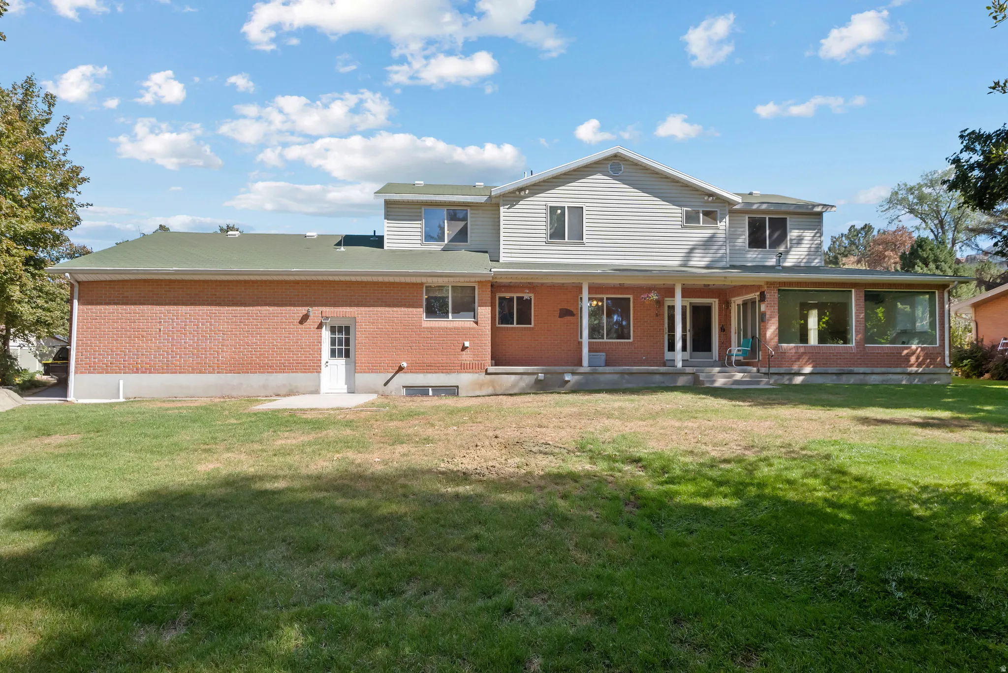 Two-story residence featuring a brick and siding exterior, expansive rear yard, covered porch, and a sunroom with large windows
