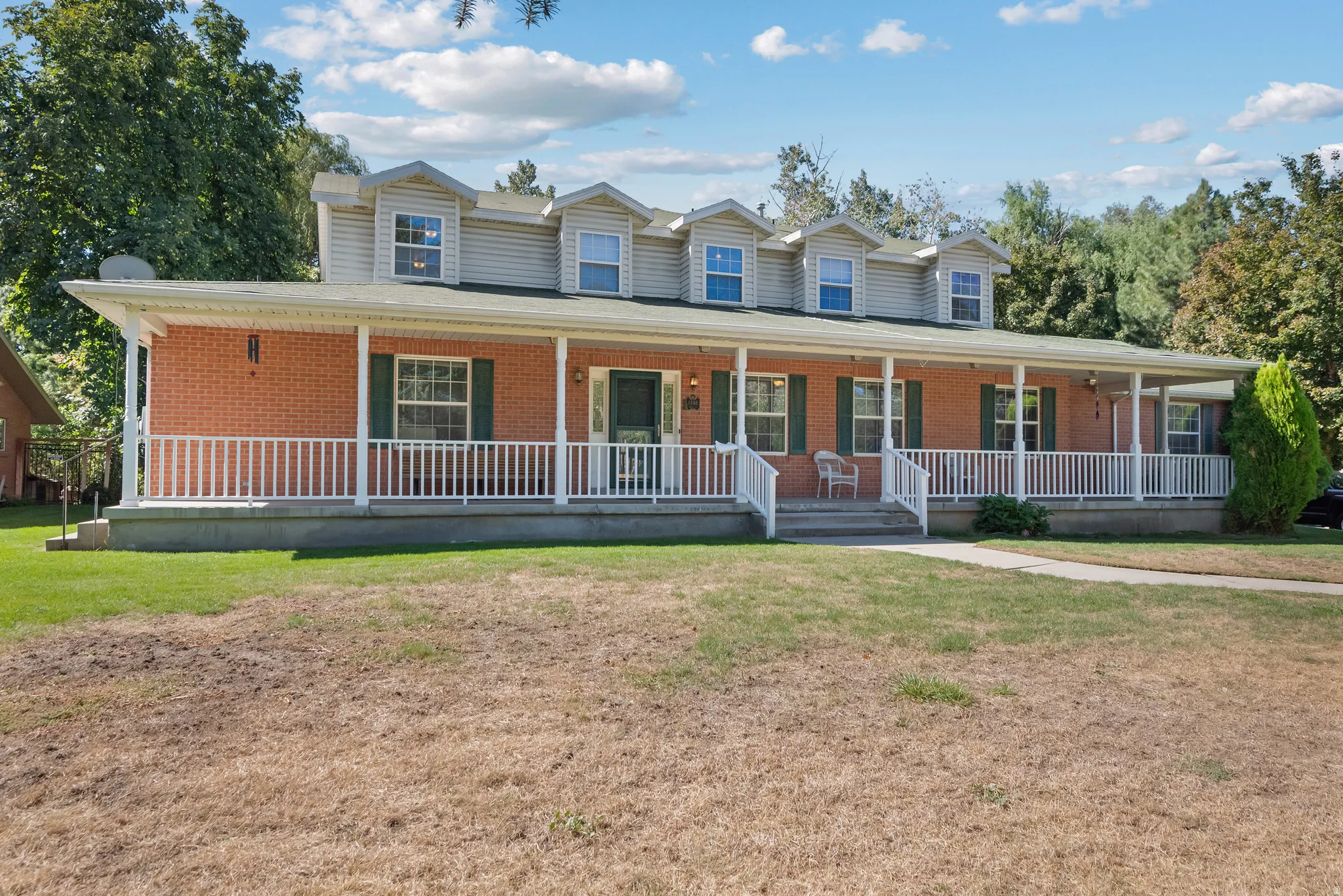 Brick exterior with a full-width covered porch, multiple dormer windows, and white porch railings