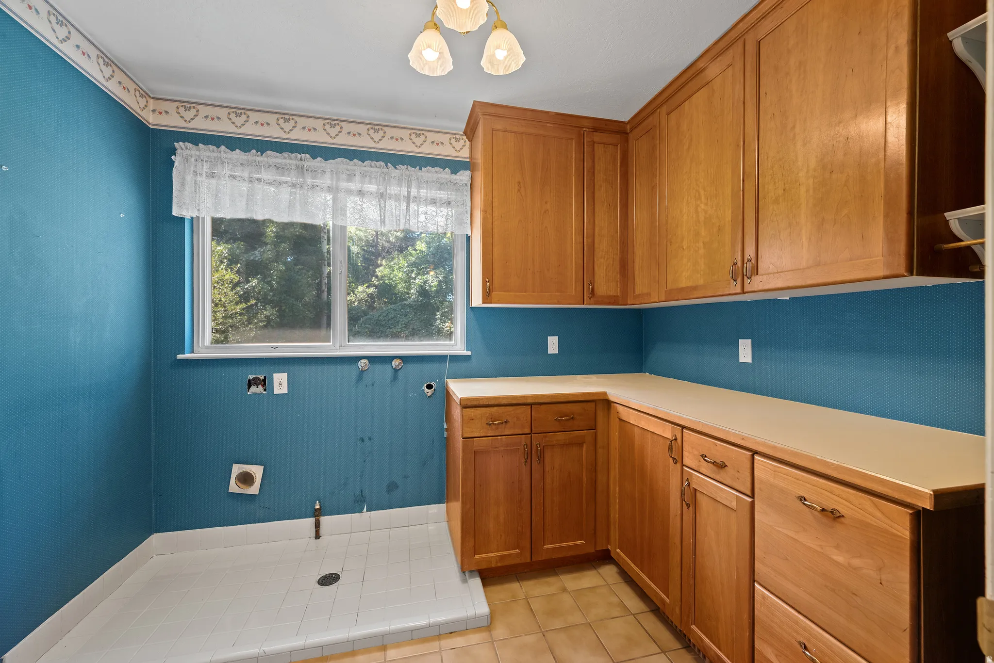 Built-in cabinetry with wood-finish doors, ample countertop space, a window, overhead lighting, and tile flooring