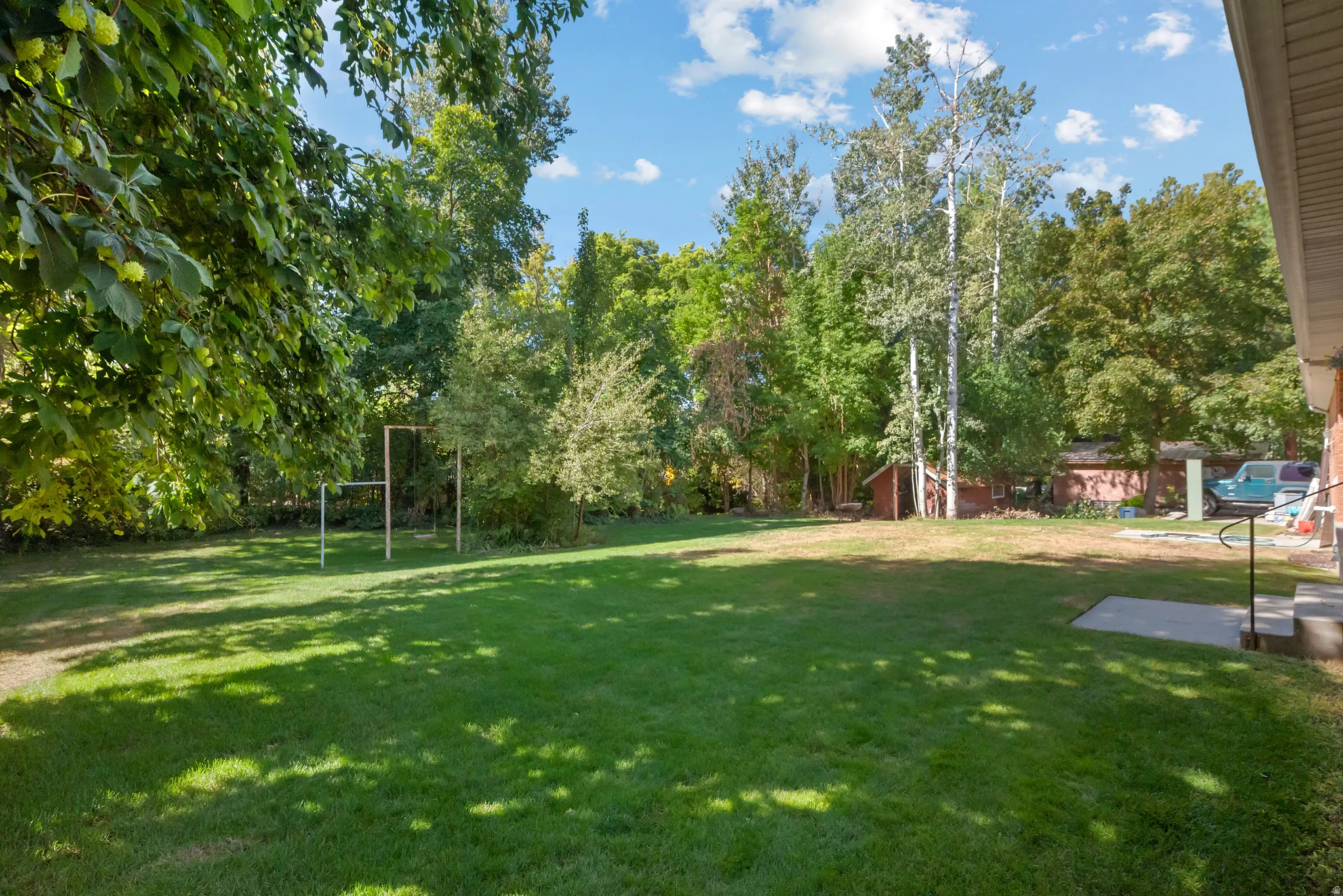 Expansive grassy yard with mature trees and a concrete patio
