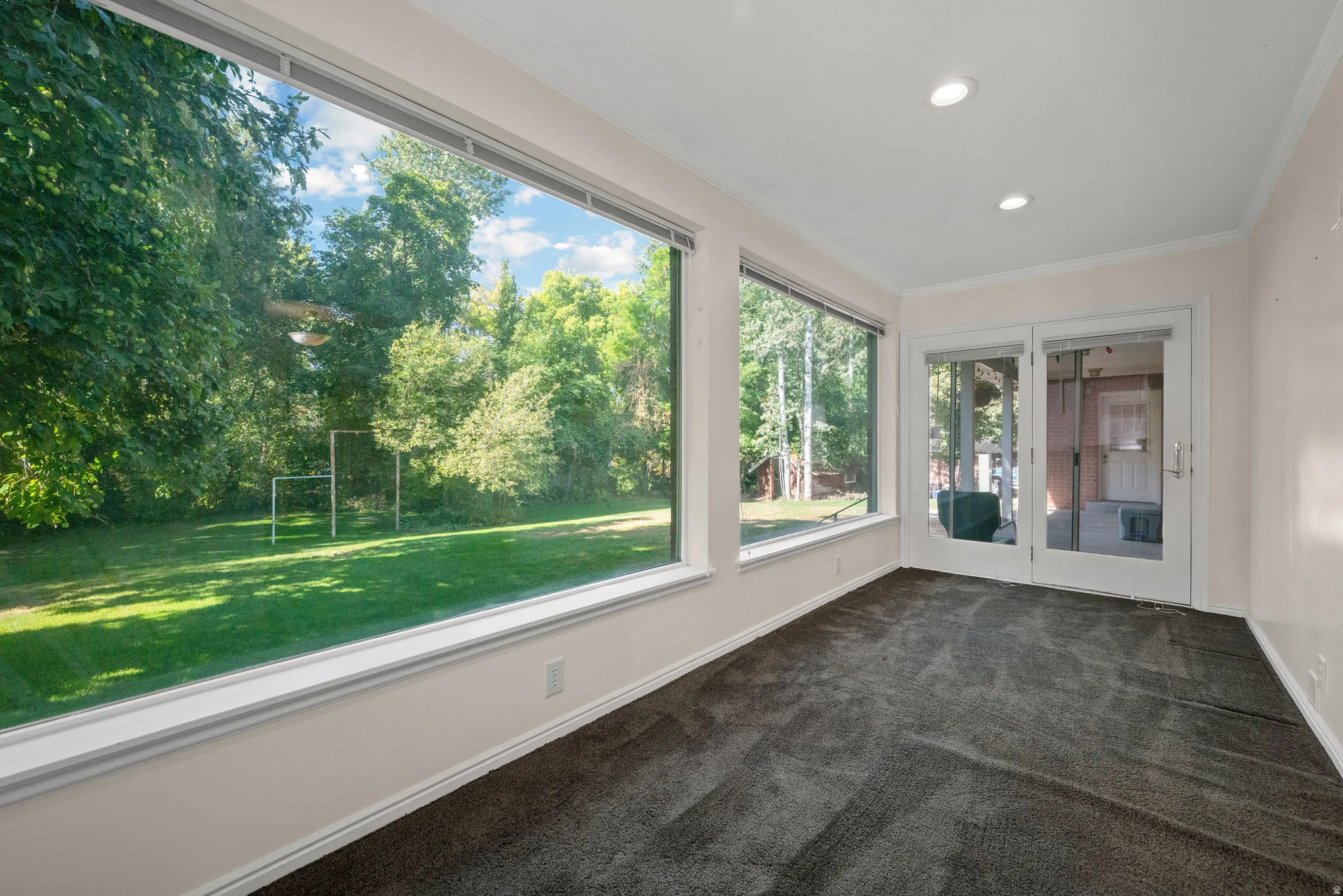 Expansive full-height windows, dark gray carpeting, recessed ceiling lighting, crown molding, and double glass-paneled doors