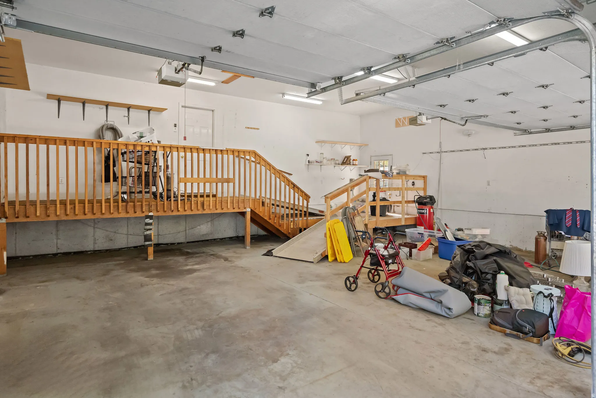 Concrete flooring garage with an elevated wood deck and ramp, overhead lighting, and white walls