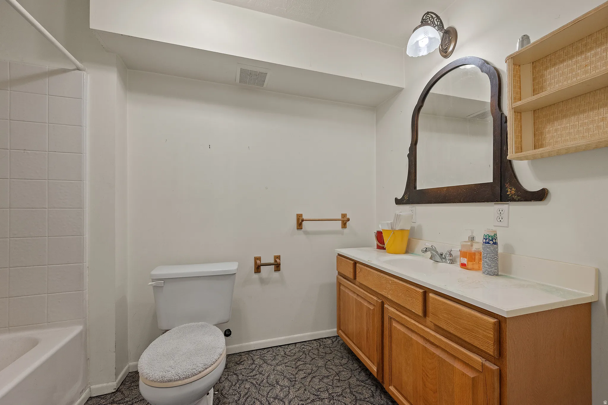 Vanity with a white countertop and wood-finish cabinetry, bathtub with white subway tile surround, wall-mounted mirror, and overhead lighting