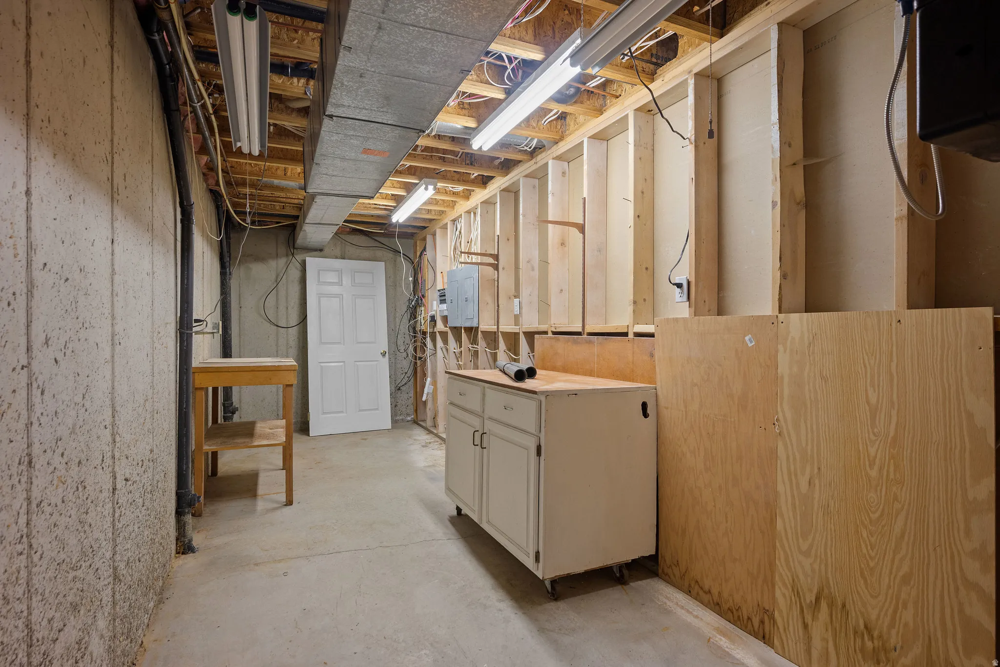 Unfinished basement with concrete flooring, exposed ceiling joists, and fluorescent lighting