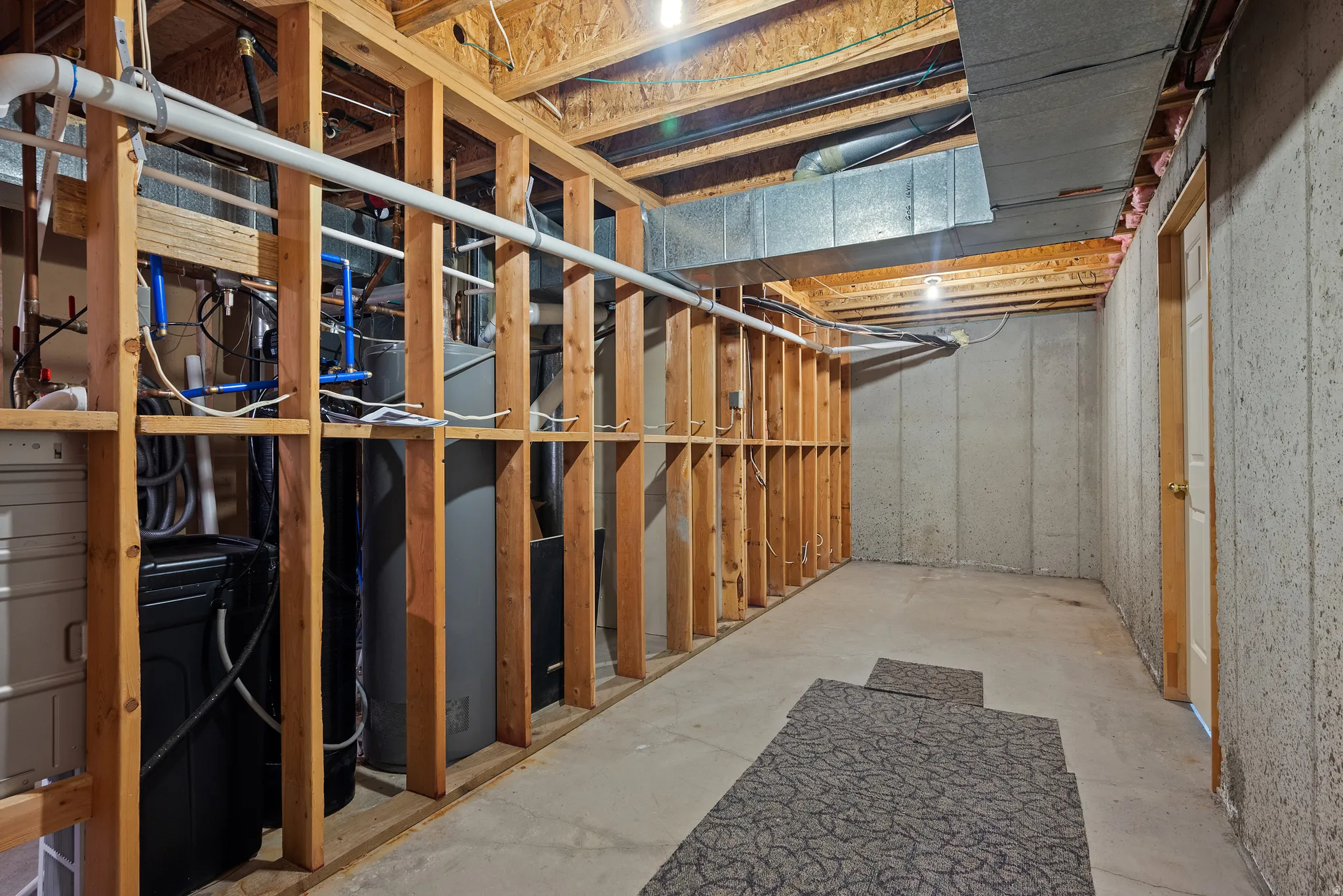 Unfinished basement space featuring exposed wooden framing, concrete flooring, and utilities