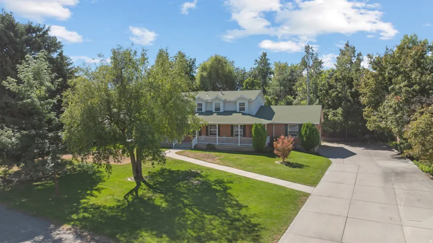 Traditional style residence featuring a light-colored exterior, an expansive front lawn, a mature tree, a long driveway, and a covered front porch
