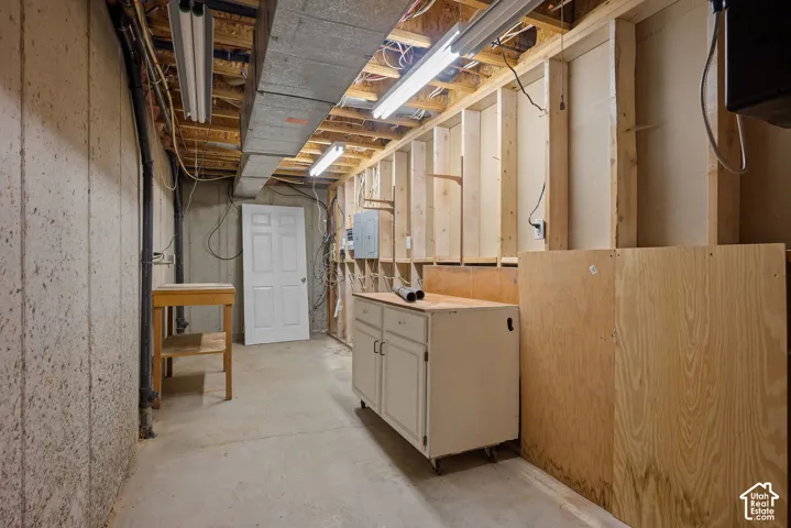 Unfinished basement with concrete flooring, exposed ceiling joists, and fluorescent lighting