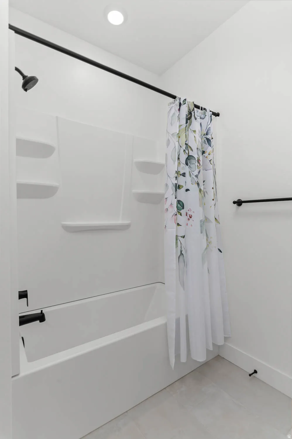 White bathtub with a shower combination, featuring matte black fixtures and a recessed ceiling light