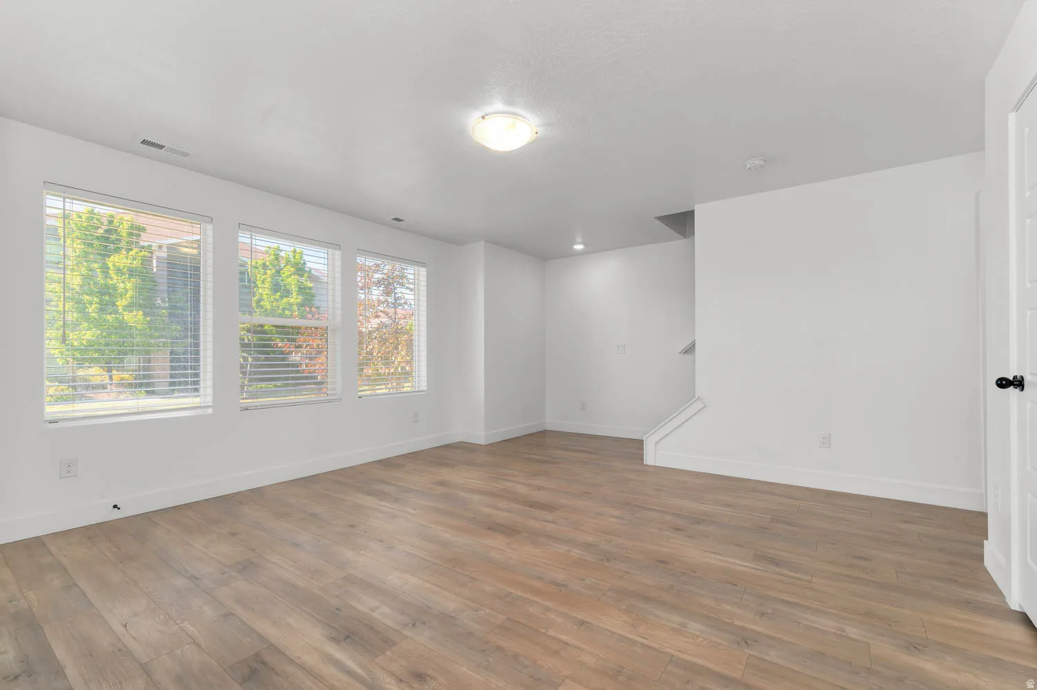 Expansive room featuring multiple windows, wood-finish flooring, a built-in staircase, and a flush-mount ceiling light