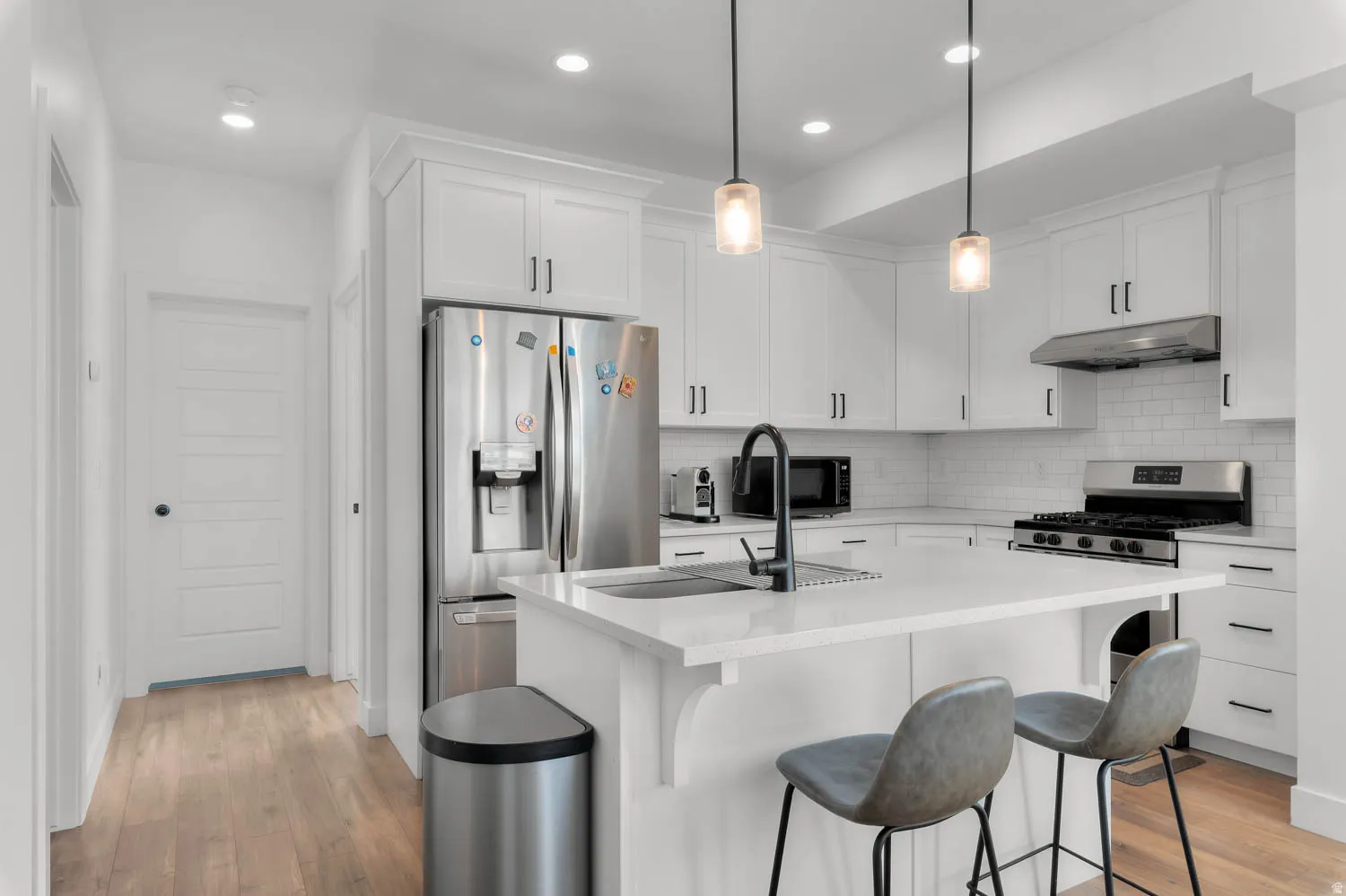 White shaker cabinetry, stainless steel appliances, subway tile backsplash, recessed lighting, and wood-finish flooring