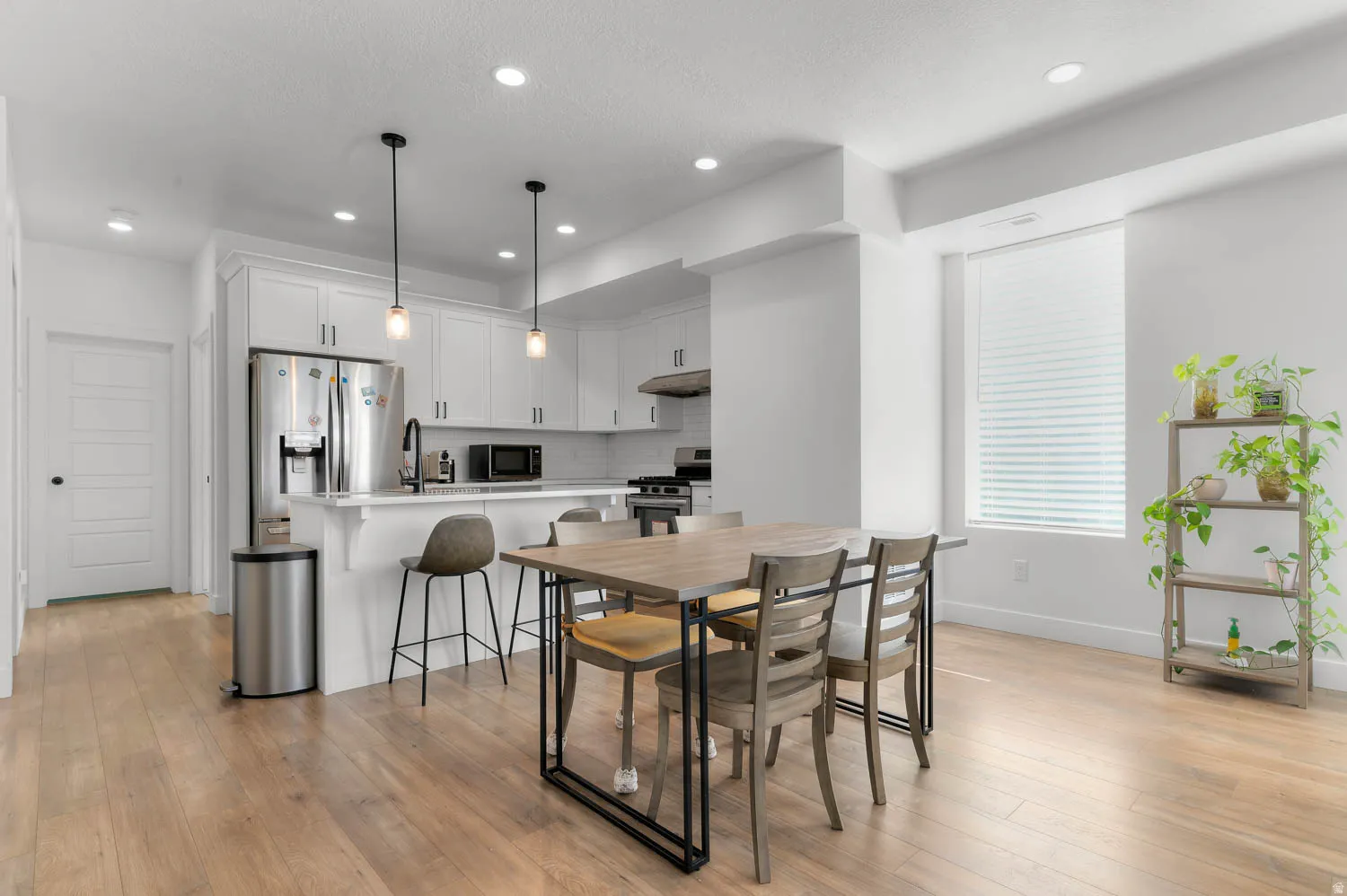 Open-concept kitchen and dining area featuring white cabinetry, stainless steel appliances, a kitchen island, and wood-finish flooring