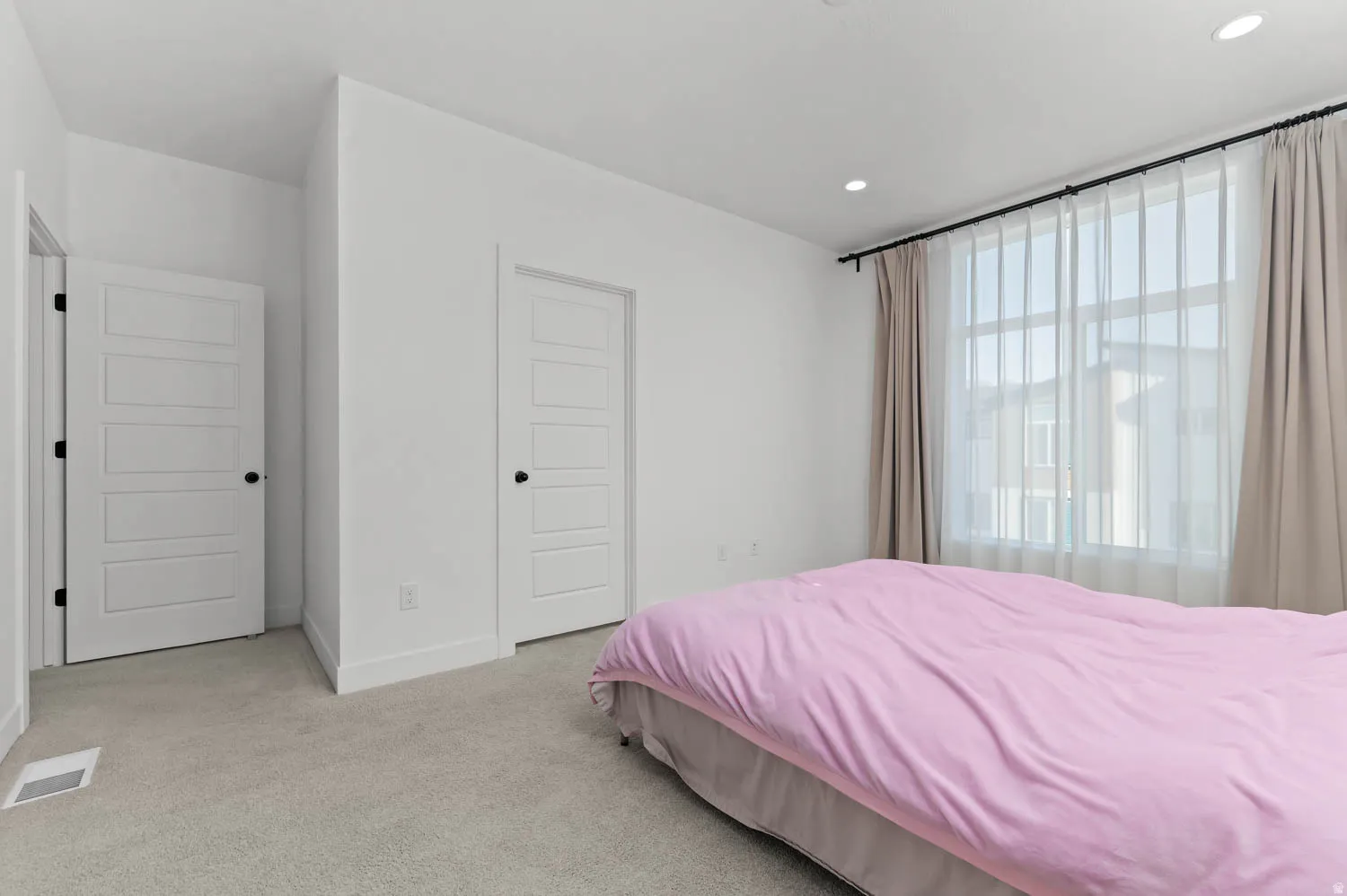 Wall-to-wall carpeting, recessed ceiling lighting, and a large window with curtain rods