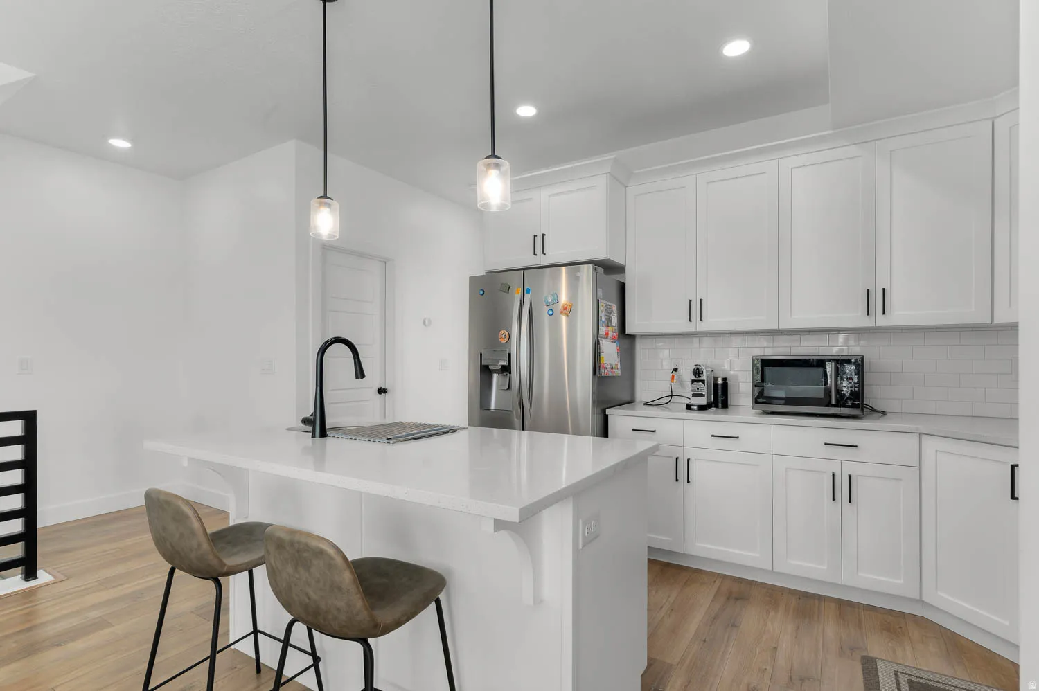 Kitchen featuring white shaker cabinetry, subway tile backsplash, a stainless steel refrigerator, and an island with a matte black faucet