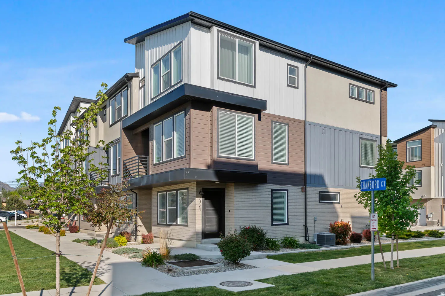 Modern multi-story exterior with varied siding materials, prominent black-trimmed windows, and a paved walkway leading to the entrance