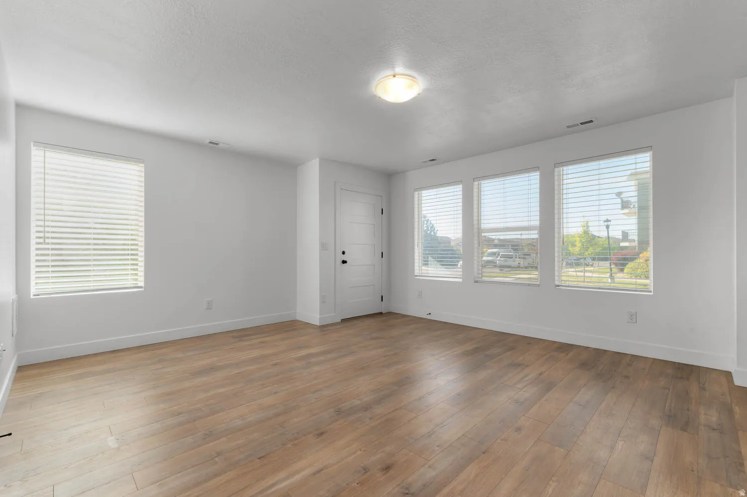 Wood-finish flooring, white walls, multiple windows with blinds, recessed lighting, and a paneled door