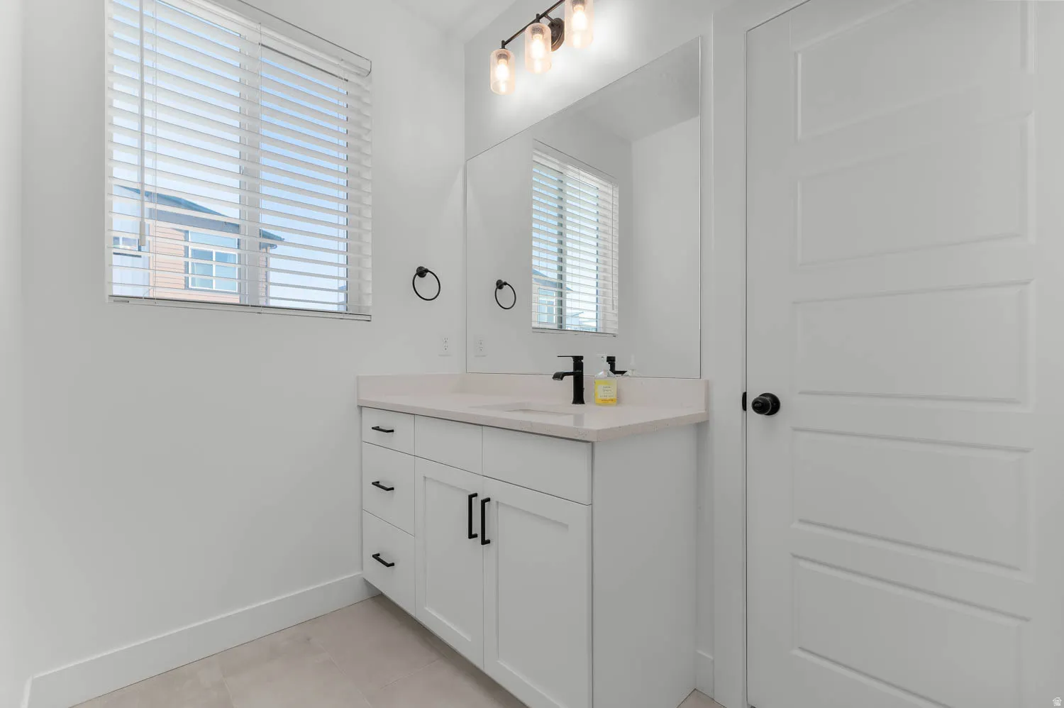 White shaker-style vanity with a light-toned countertop, matte black faucet, and a large mirror