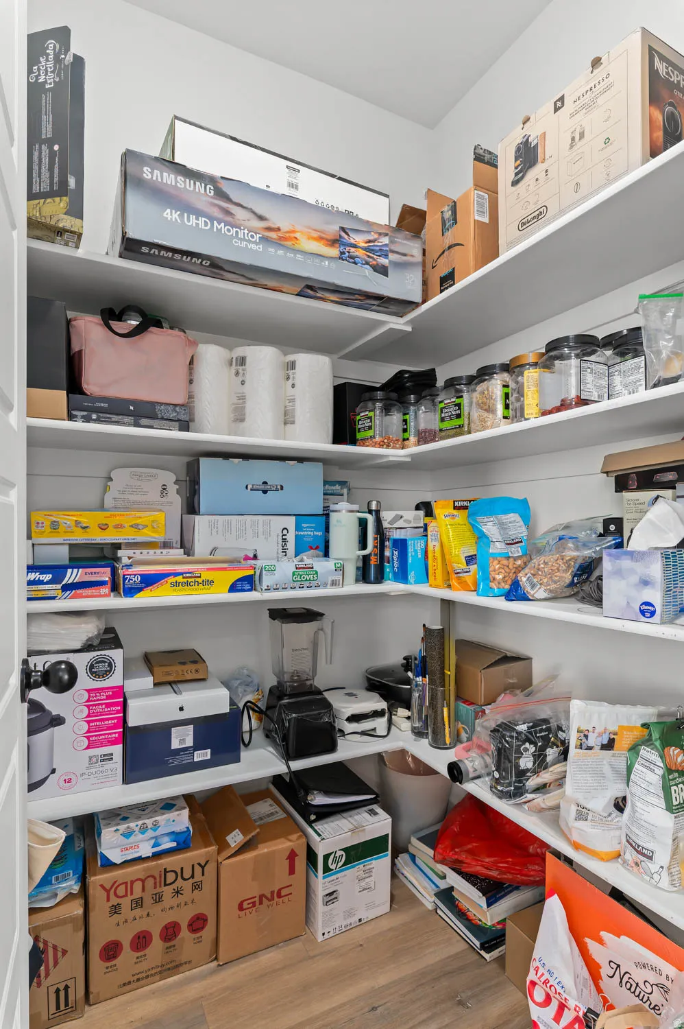 Walk-in pantry featuring white shelving, light wood-finish flooring, and ample storage space