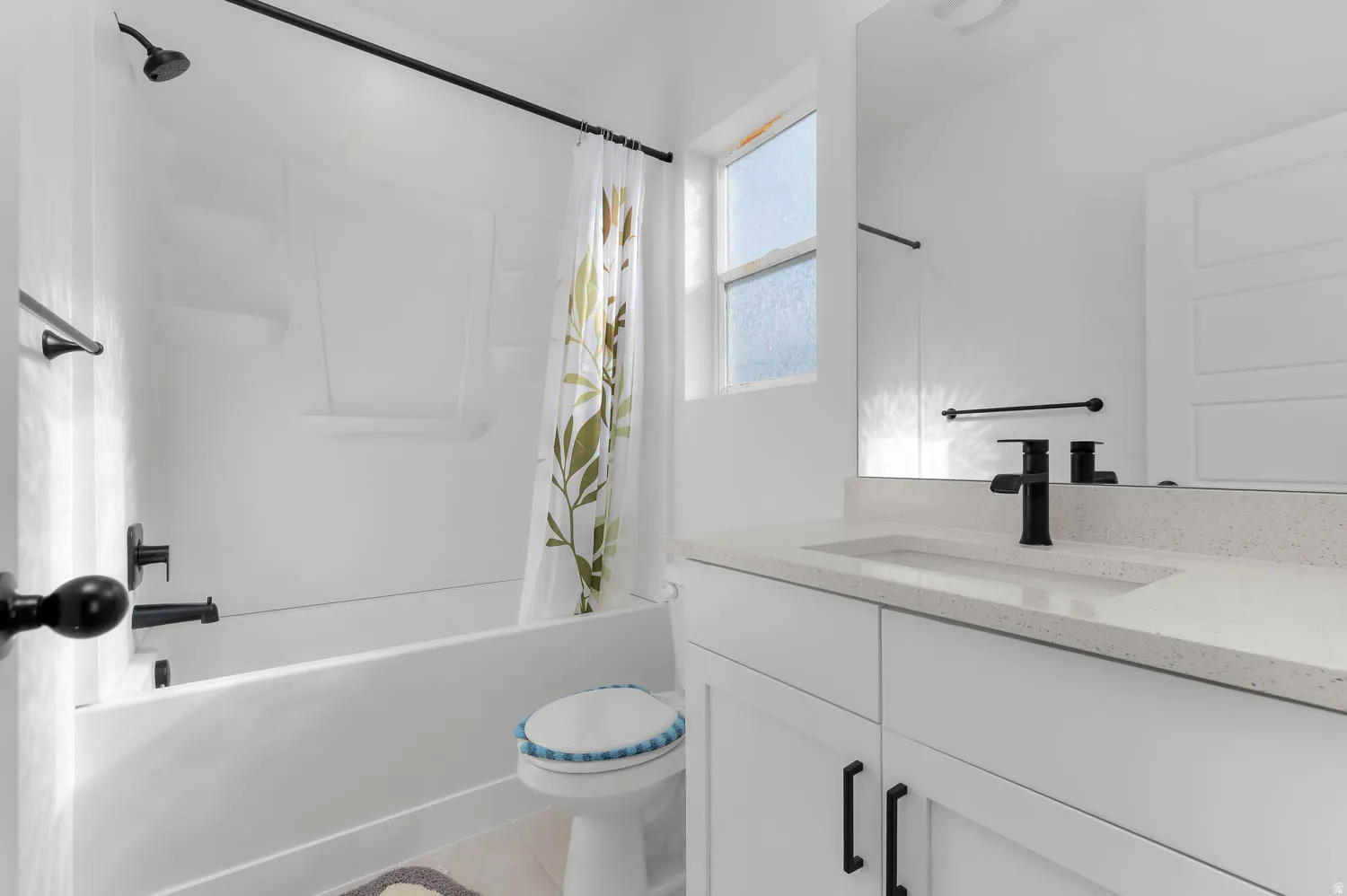 White shower/tub combination with black fixtures, vanity with integrated sink, white countertop, and full-width mirror