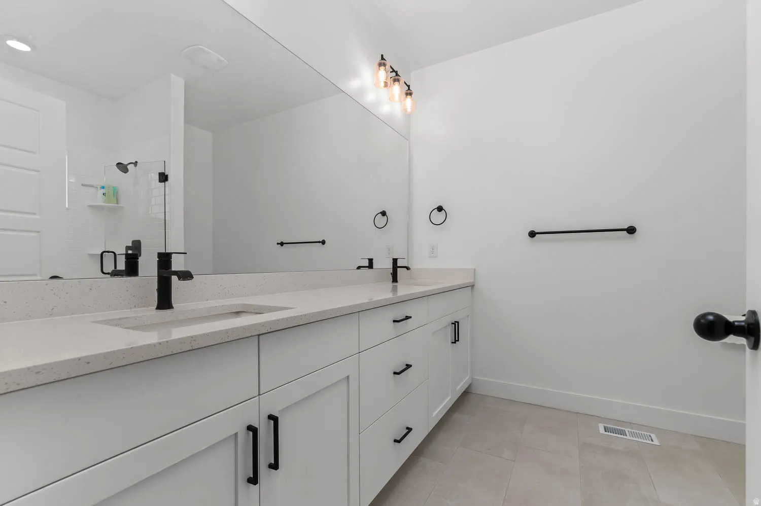 Dual sink vanity with white cabinetry, light-toned countertop, and matte black fixtures