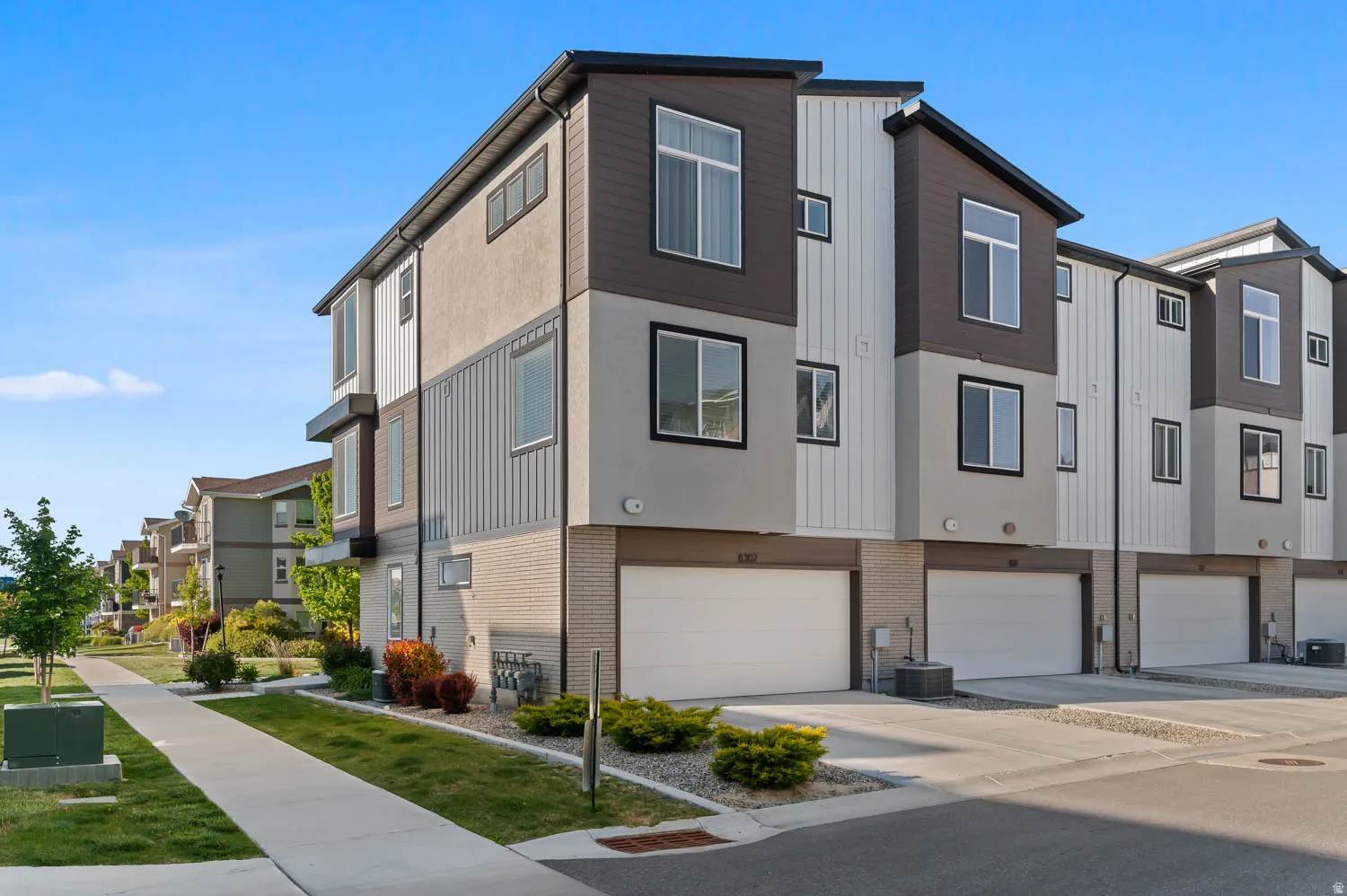 Contemporary exterior featuring a multi-tone facade, prominent windows, attached garage, and manicured landscaping
