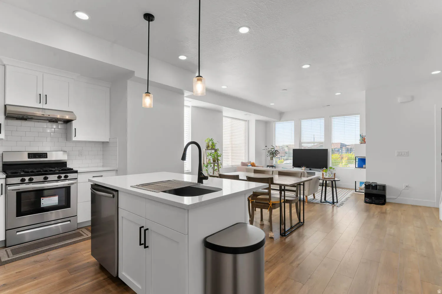 Open-concept living space with wood-finish flooring, white cabinetry, stainless steel appliances, and an integrated kitchen island with a sink