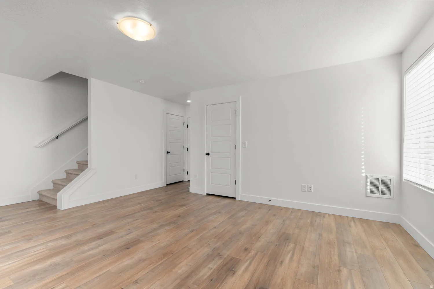 Wood-finish flooring, white walls, and a staircase with a carpeted tread