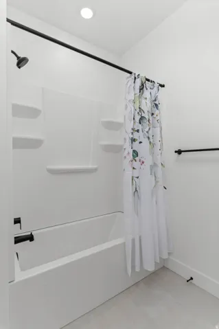 White bathtub with a shower combination, featuring matte black fixtures and a recessed ceiling light