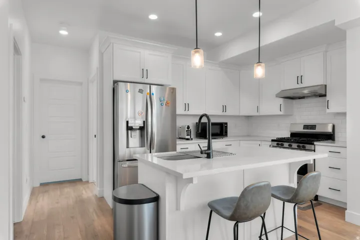 White shaker cabinetry, stainless steel appliances, subway tile backsplash, recessed lighting, and wood-finish flooring