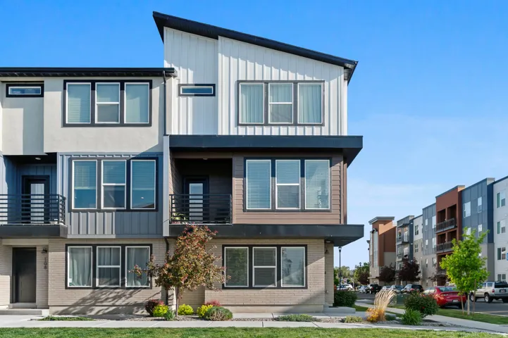 Modern three-story townhouse featuring a multi-textured facade, an asymmetrical roofline, and multiple black-framed windows