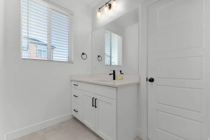 White shaker-style vanity with a light-toned countertop, matte black faucet, and a large mirror