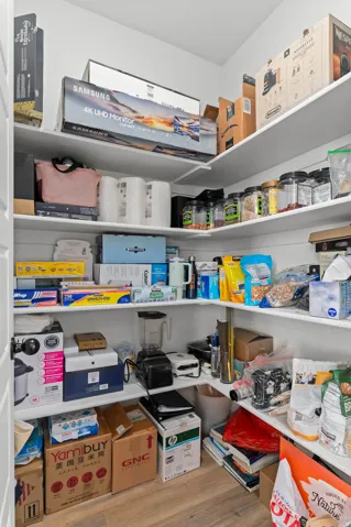 Walk-in pantry featuring white shelving, light wood-finish flooring, and ample storage space