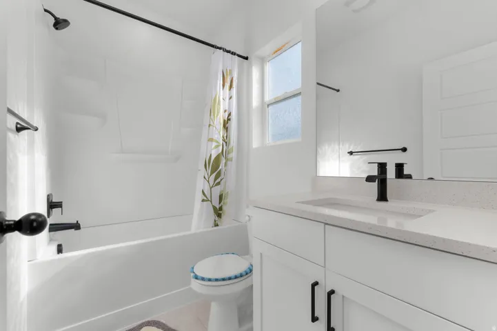 White shower/tub combination with black fixtures, vanity with integrated sink, white countertop, and full-width mirror