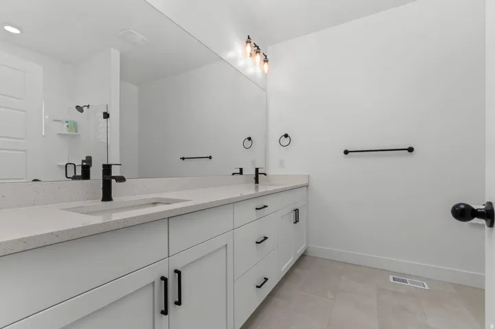 Dual sink vanity with white cabinetry, light-toned countertop, and matte black fixtures