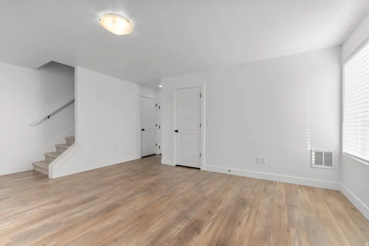 Wood-finish flooring, white walls, and a staircase with a carpeted tread