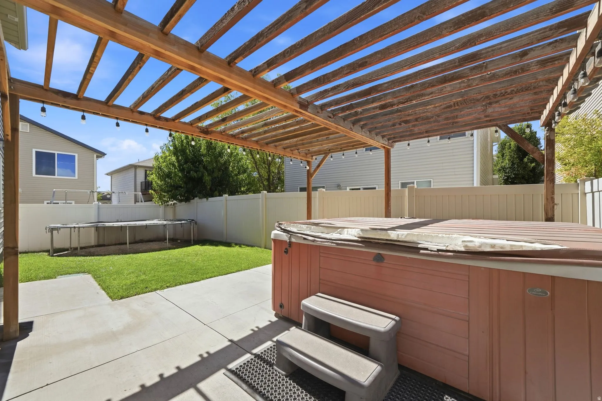 Expansive concrete patio with a wooden pergola, leading to a manicured lawn and a privacy fence