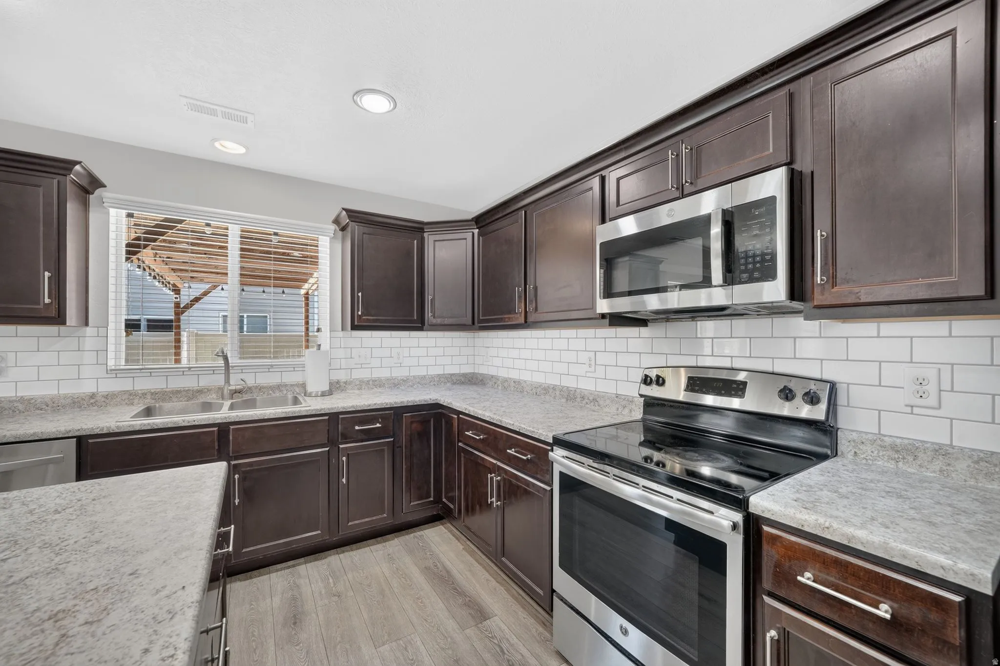 Dark wood cabinetry, light-toned countertops, white subway tile backsplash, stainless steel appliances, and wood-finish flooring