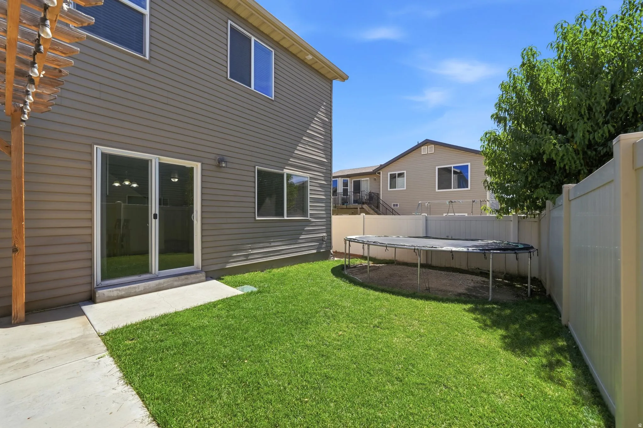 Expansive grassy backyard featuring a concrete patio, sliding glass door access, and privacy fencing