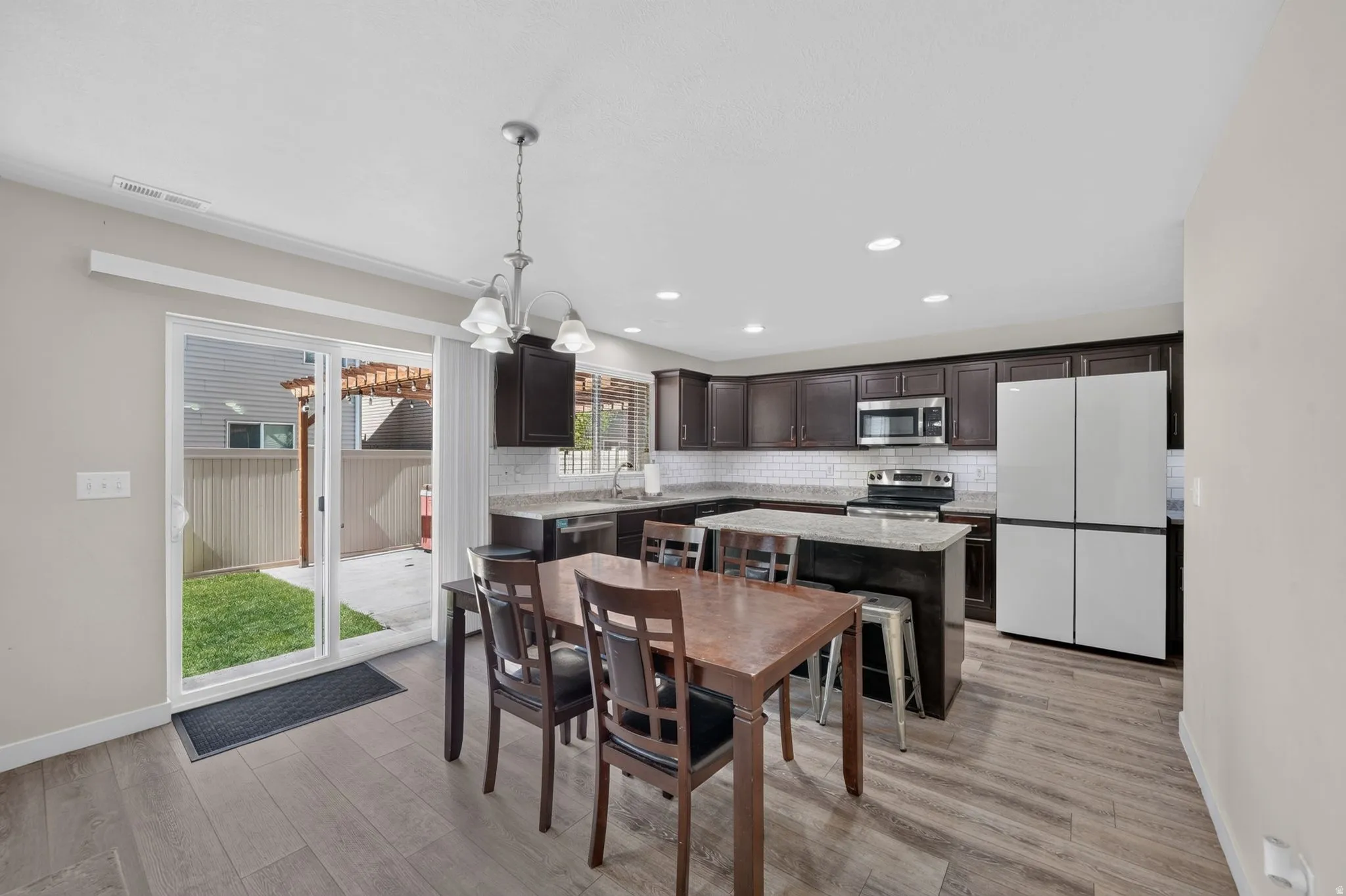 Open-concept kitchen featuring dark wood cabinetry, stainless steel appliances, a center island with bar seating, and wood-finish flooring