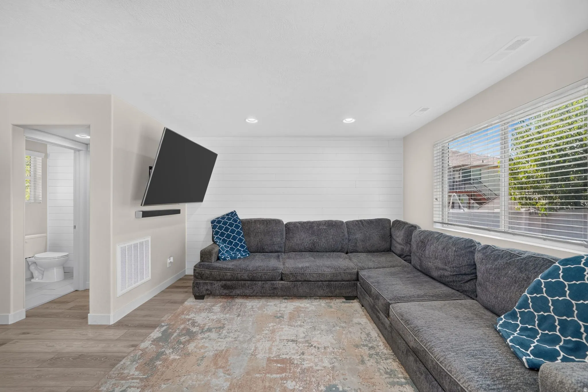 Recessed lighting, wood-finish flooring, accent wall with horizontal paneling, and a transom window with blinds