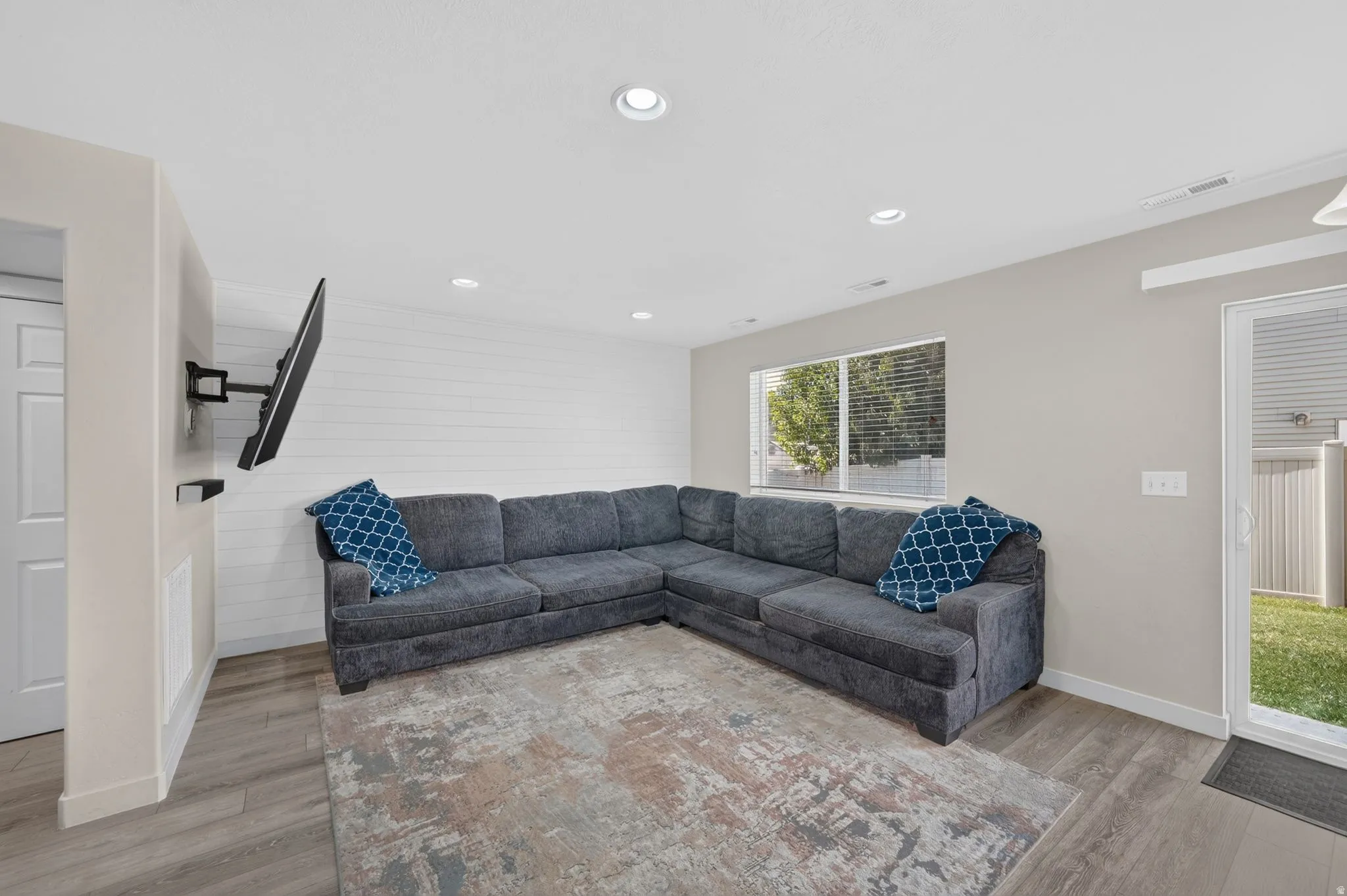 Recessed ceiling lighting, wood-finish flooring, white shiplap accent wall, white door with paneling, and a glass sliding door to the exterior