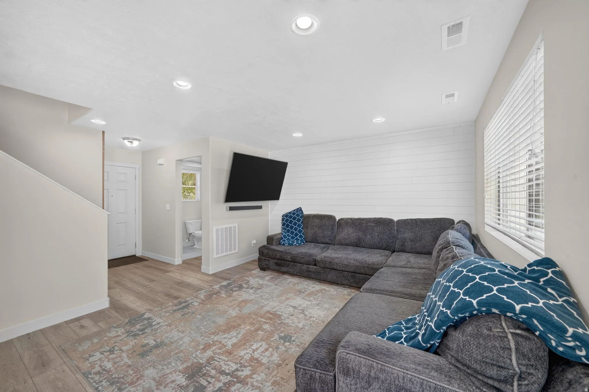 Recessed lighting, wood-finish flooring, white shiplap accent wall, white window blinds, and a white interior door